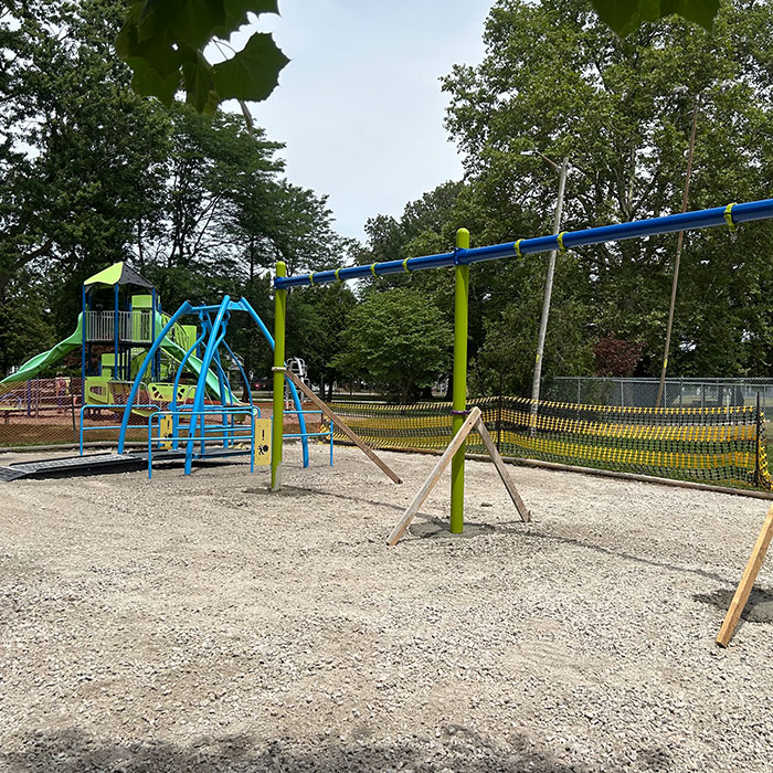 Structural assembly of a heavy-duty swing set with high-visibility green posts and blue crossbars. Allsite Services.